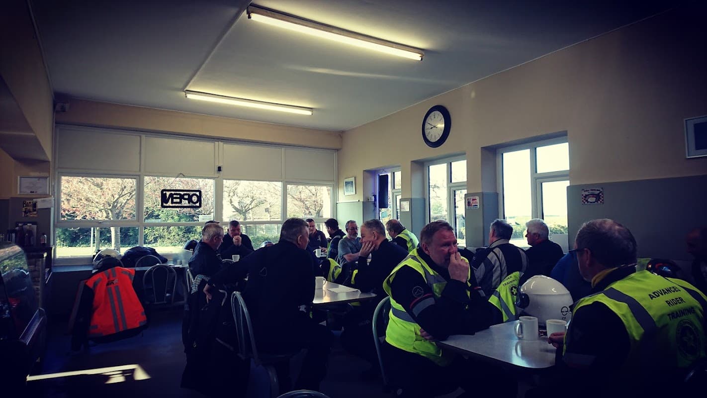 Busy cafe interior with patrons in high-visibility jackets enjoying food and drinks at tables, bright windows letting in light.