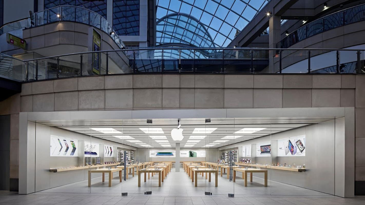Modern Apple store with wooden tables, displayed tech products, and large glass windows in a shopping center.