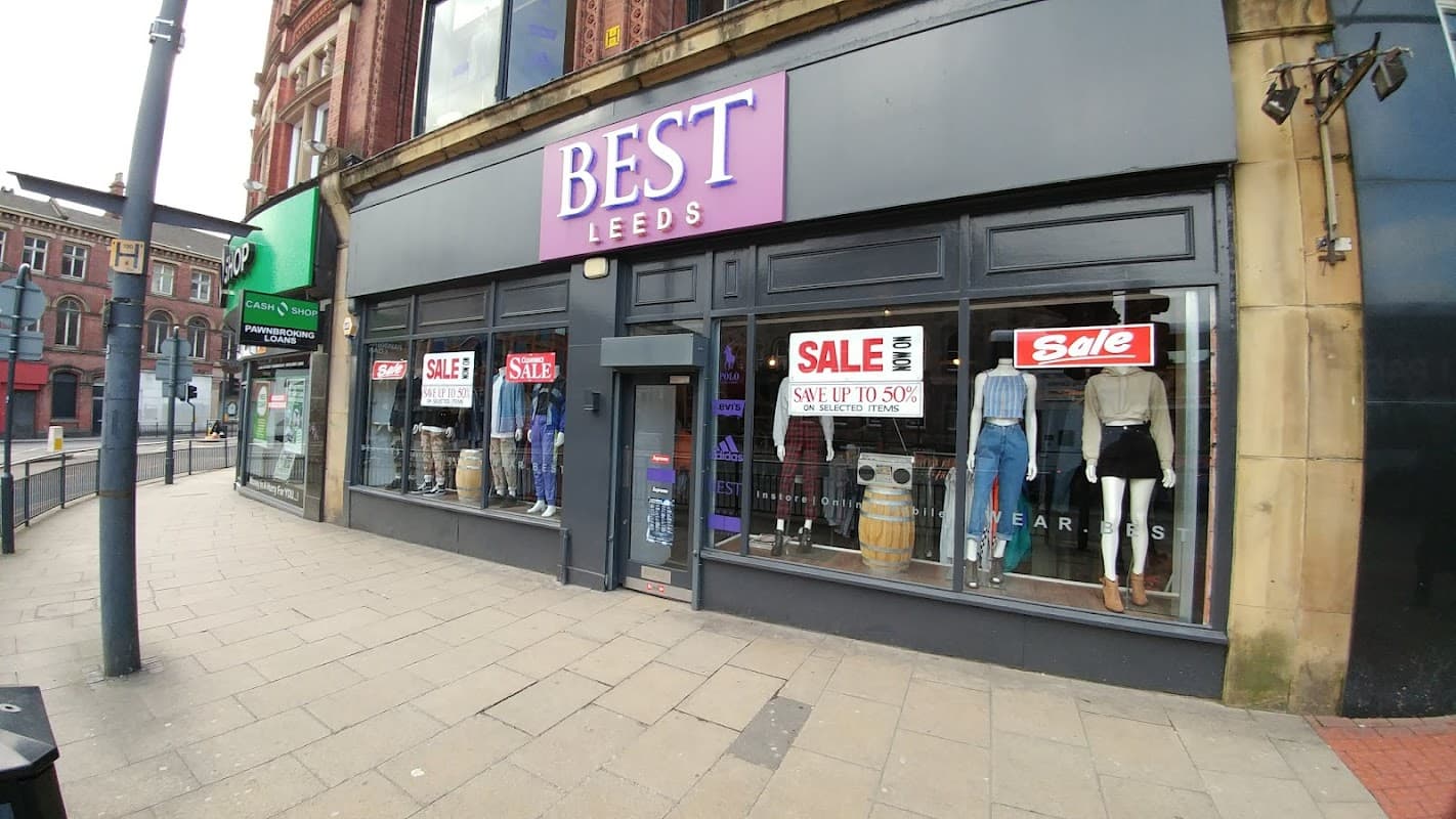 Corner shop "BEST" in Leeds with large sale signs, showcasing clothing displays and a modern storefront design.