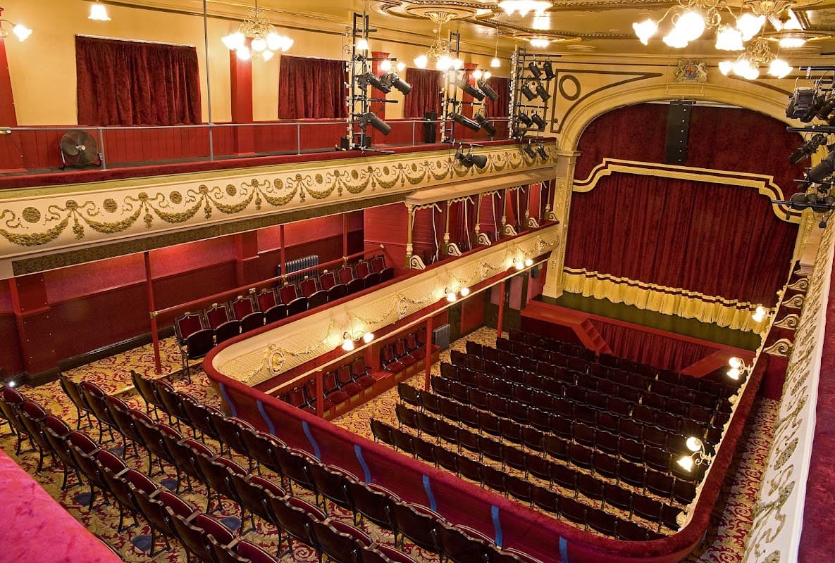 Interior of City Varieties Music Hall featuring red velvet seats, ornate decor, and a stage with golden accents.
