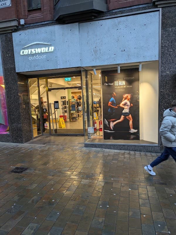 Cotswold Outdoor shop front with large window display featuring running apparel and a person walking by on the street.