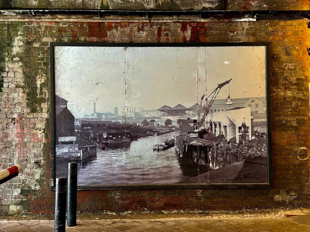 Historic black-and-white photo of a canal and warehouse, framed against a brick wall in Granary Wharf Parking.