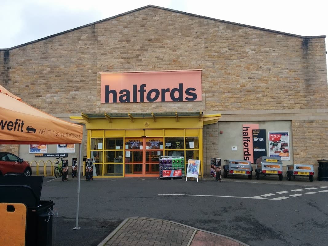 Halfords store exterior in Kirkstall, Leeds, featuring large signage, parking area, and promotional banners.