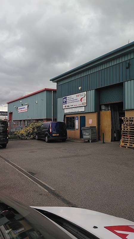 Industrial building with blue and red exterior, signage for IPC Fixings, parked van, and pallets outside.