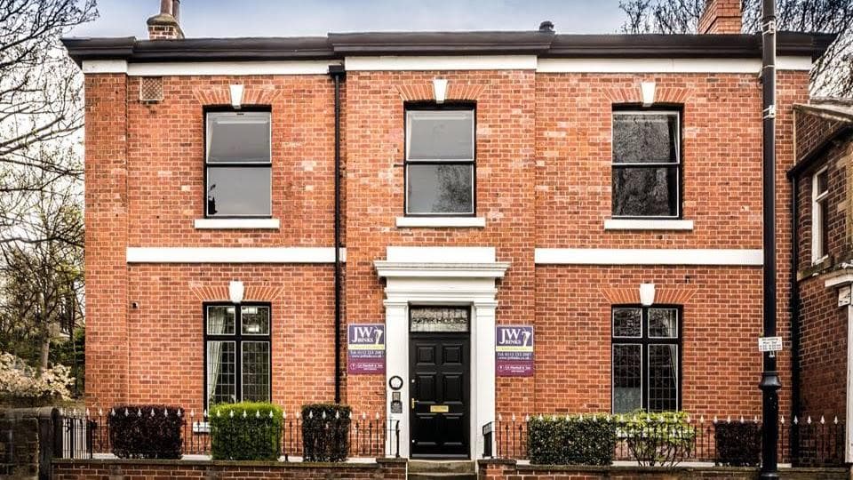 Brick building with large windows, black front door, and signs for J W Binks Funeral Directors in Leeds, Yorkshire.