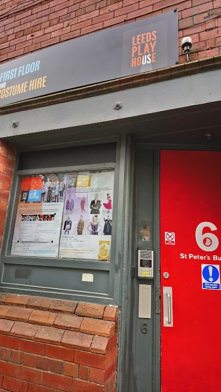 Sign for Leeds Playhouse Costume Hire above a red door, with a display of costumes and event posters in the window.