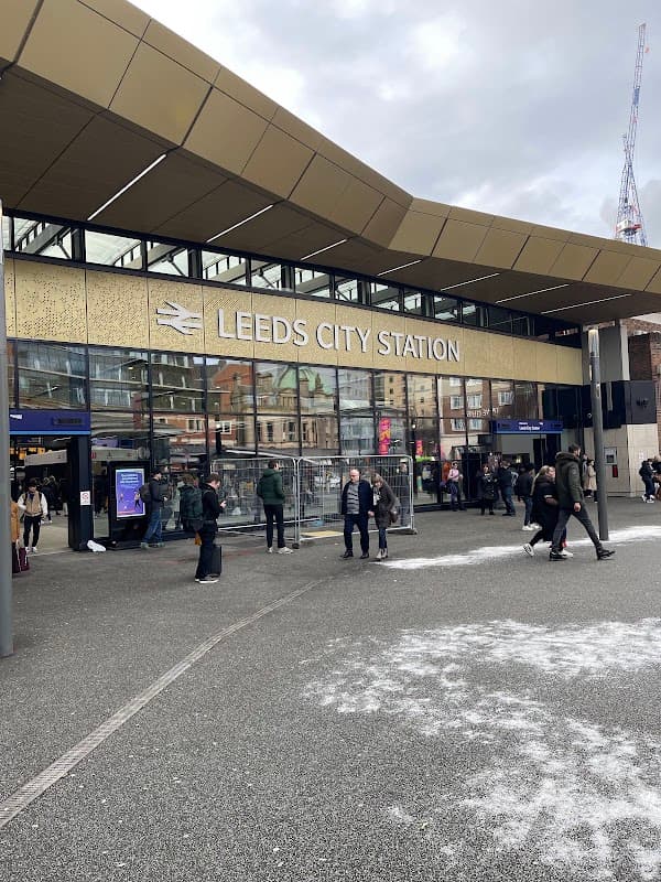 Leeds City Station entrance with people, modern architecture, and signage, set against a cloudy sky.