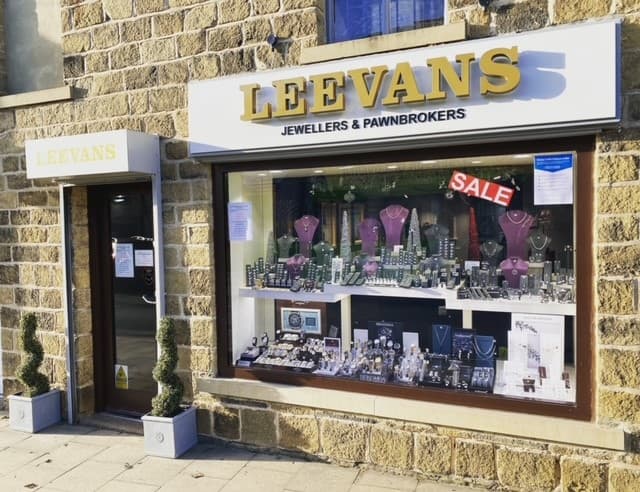 Jewellery shop display featuring necklaces, watches, and a "SALE" sign, with stone building exterior.
