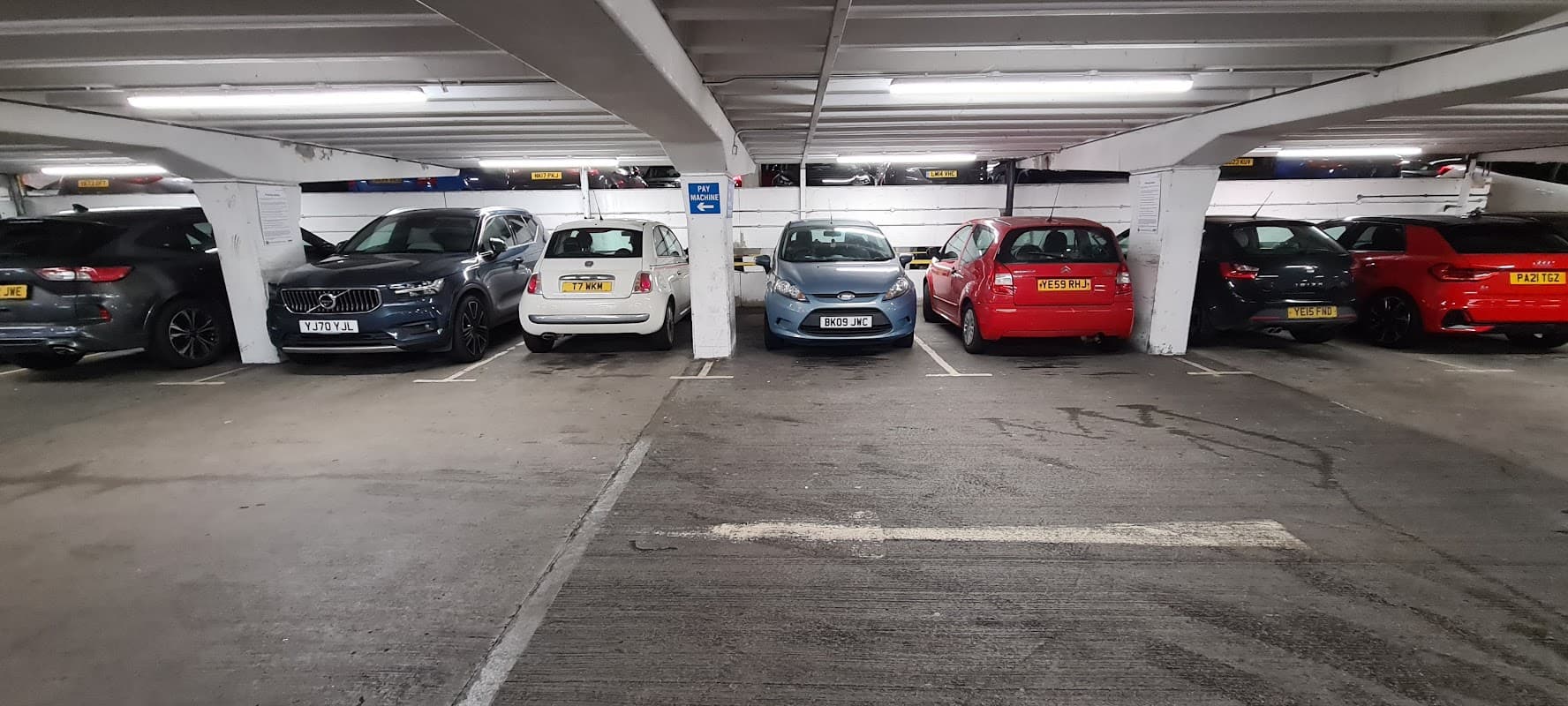 Multi-storey car park with parked vehicles, including grey, white, blue, and red cars in a well-lit underground setting.