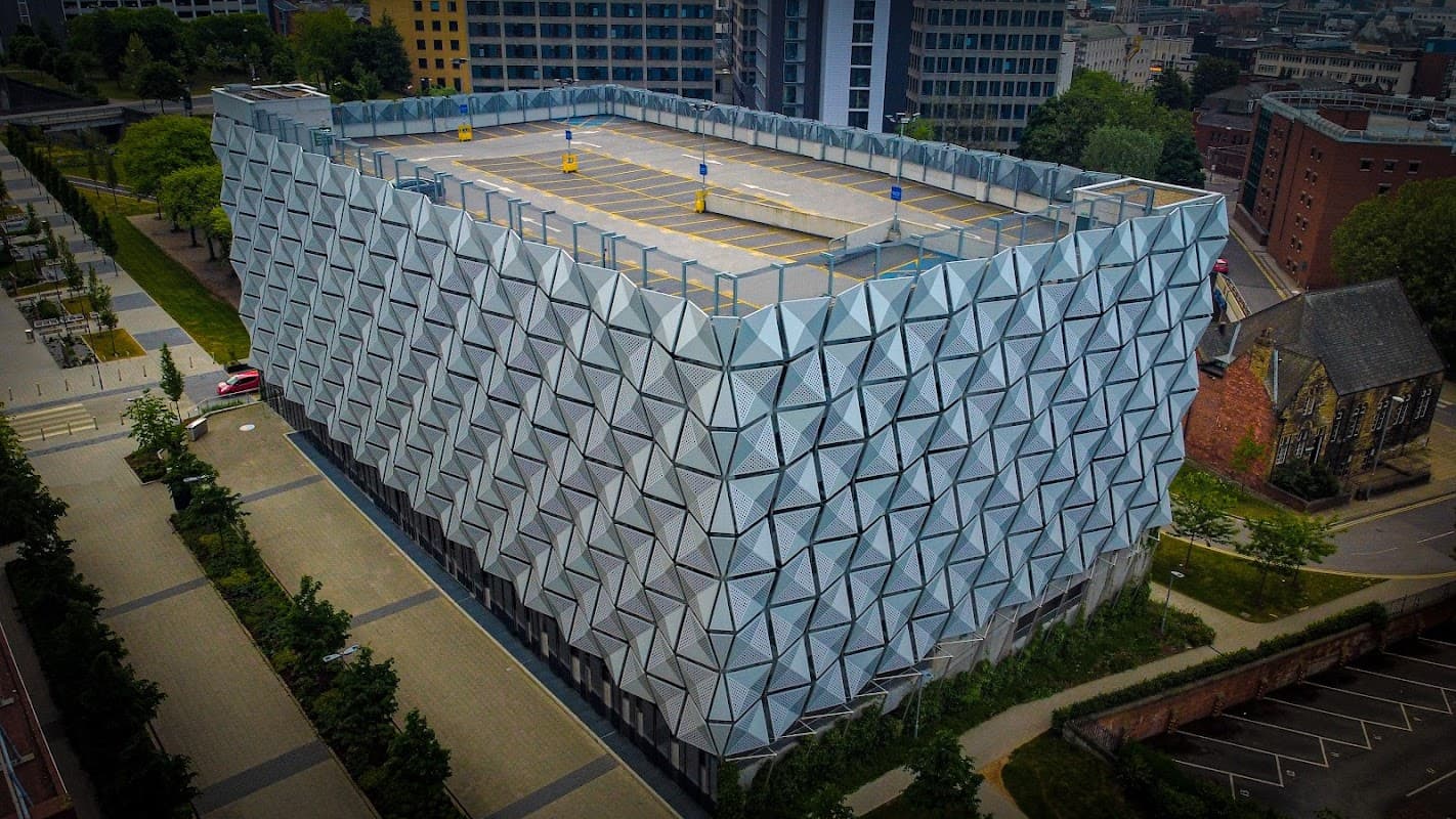 Modern multi-story car park with a geometric faΓ§ade, surrounded by greenery and urban buildings in Leeds, Yorkshire.