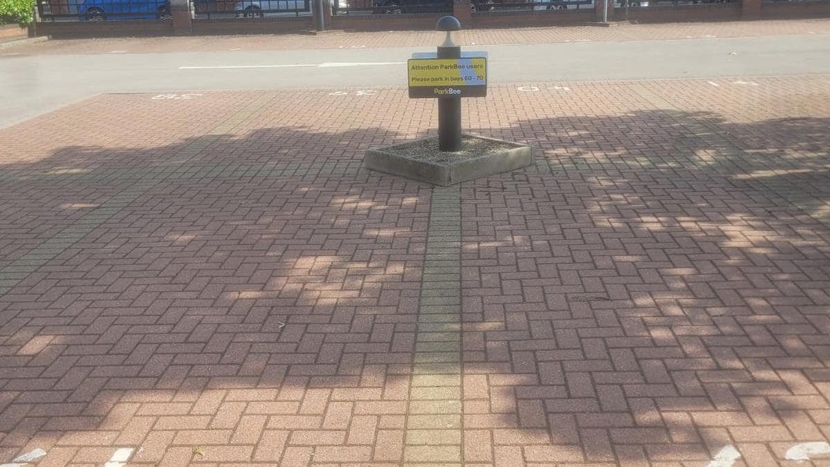 Pay & Display parking area with marked spaces and a signpost in a brick-paved lot, shaded by nearby trees.