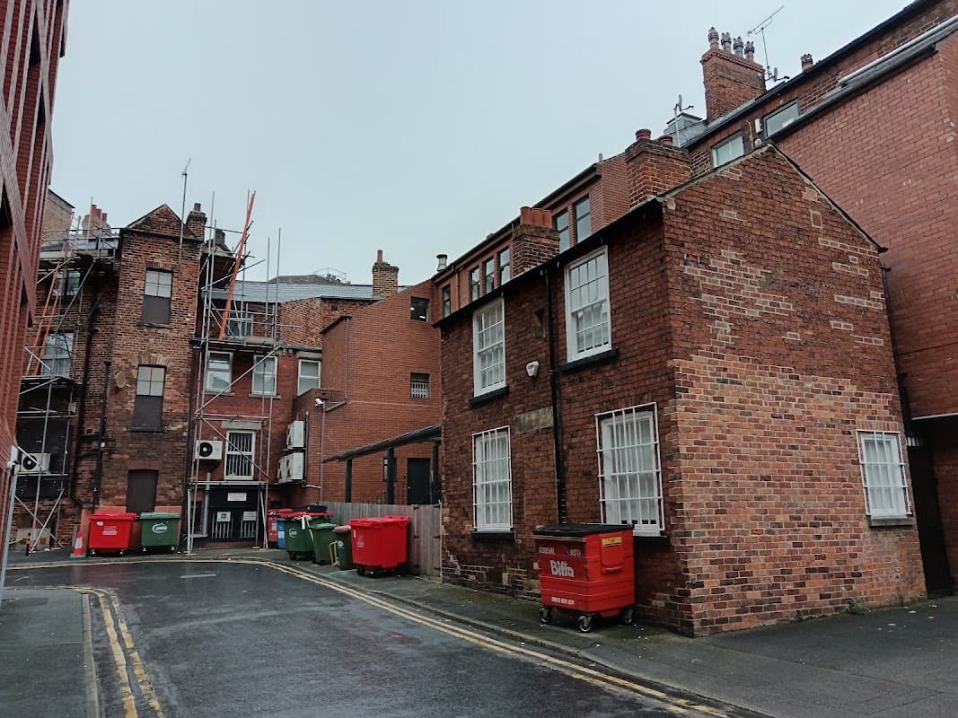 Brick buildings with white windows, red bins, and scaffolding in a narrow street in Leeds, Yorkshire.