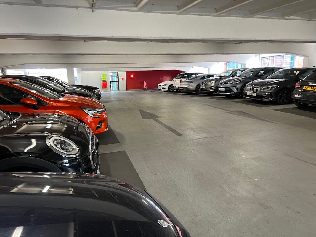 Parking garage with several parked cars, clear directional arrow, and a red wall in the background.