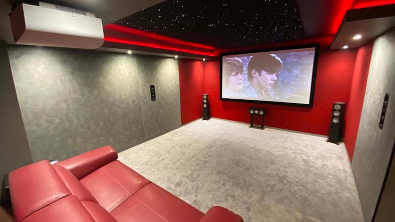 Home theater with a large screen, red accent walls, plush seating, and starry ceiling, creating a cozy atmosphere.