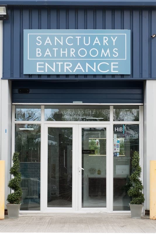Modern storefront with "Sanctuary Bathrooms" sign, glass doors, and potted plants flanking the entrance.