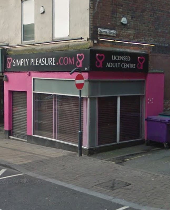 Pink storefront with "Simply Pleasure" sign, featuring closed shutters and a "Licensed Adult Centre" label.