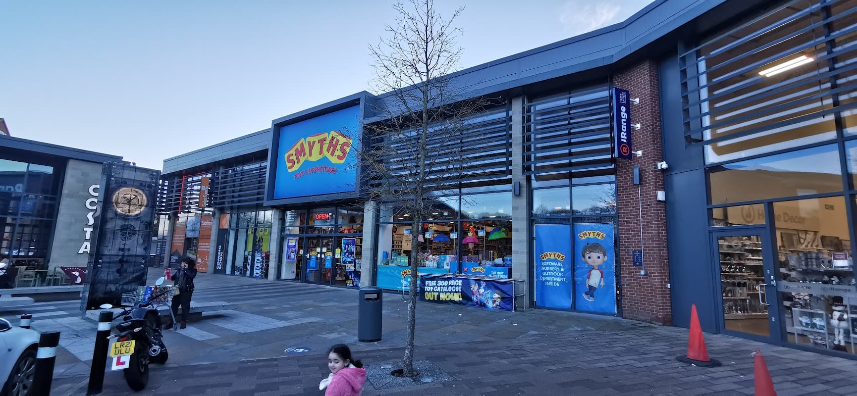 Smyths Toys Superstore entrance with colorful signage, large windows, and a child walking by on the plaza.