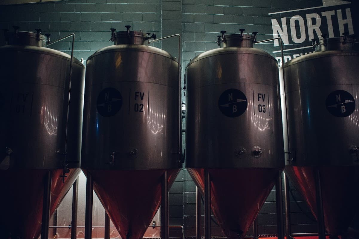 Three large metallic fermentation tanks with labels FV 01, FV 02, and FV 03, against a dark wall with "NORTH" text.