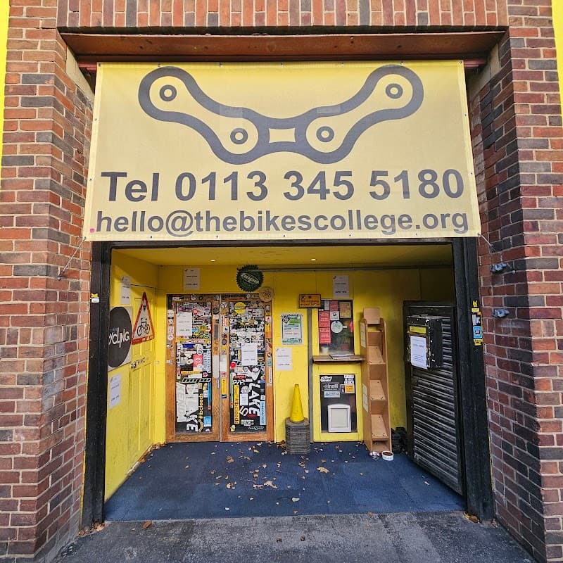 Bright yellow entrance with a large bike chain graphic, contact info, and various stickers on the door in Leeds.