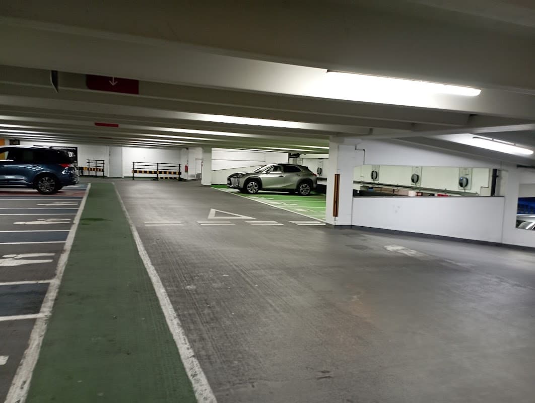 Empty car park with parked cars, green and white lines marking spaces, and overhead lighting illuminating the area.