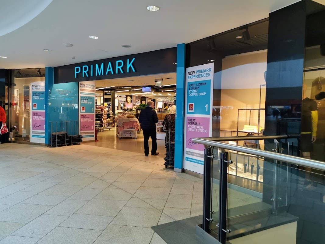 Entrance to Primark featuring large signage and a shopper walking inside, with a modern, tiled floor.