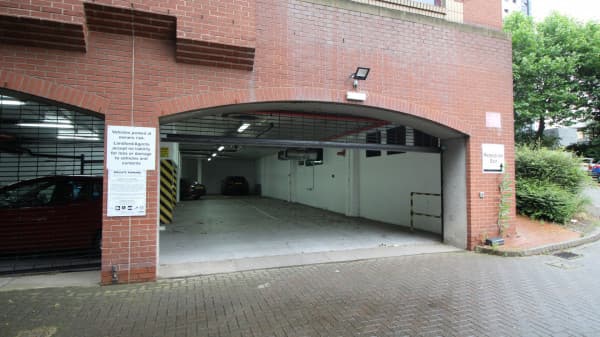 Pay & Display parking entrance with signage, brick walls, and a vacant parking area in Leeds, Yorkshire.