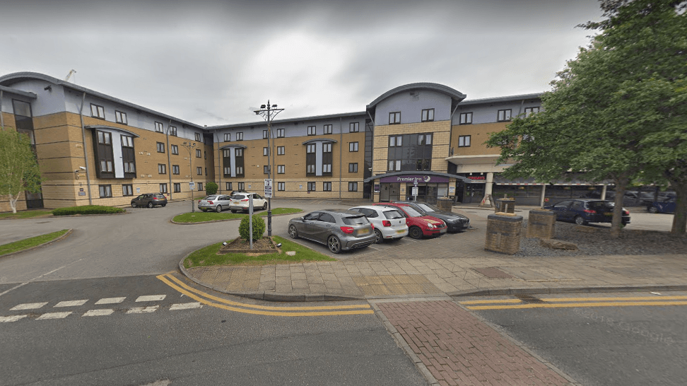 Premier Inn Leeds car park with several parked cars and a modern building surrounded by greenery.