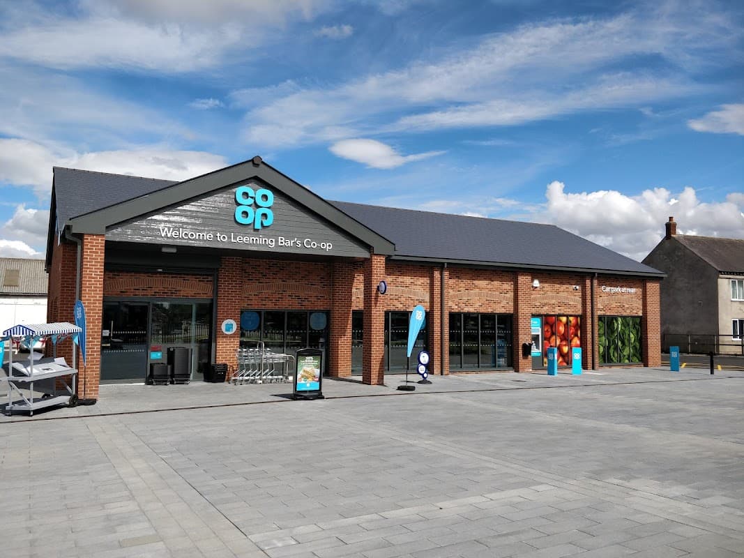 Modern brick grocery store with large windows, blue signage, and a paved entrance area in Leeming Bar, Yorkshire.
