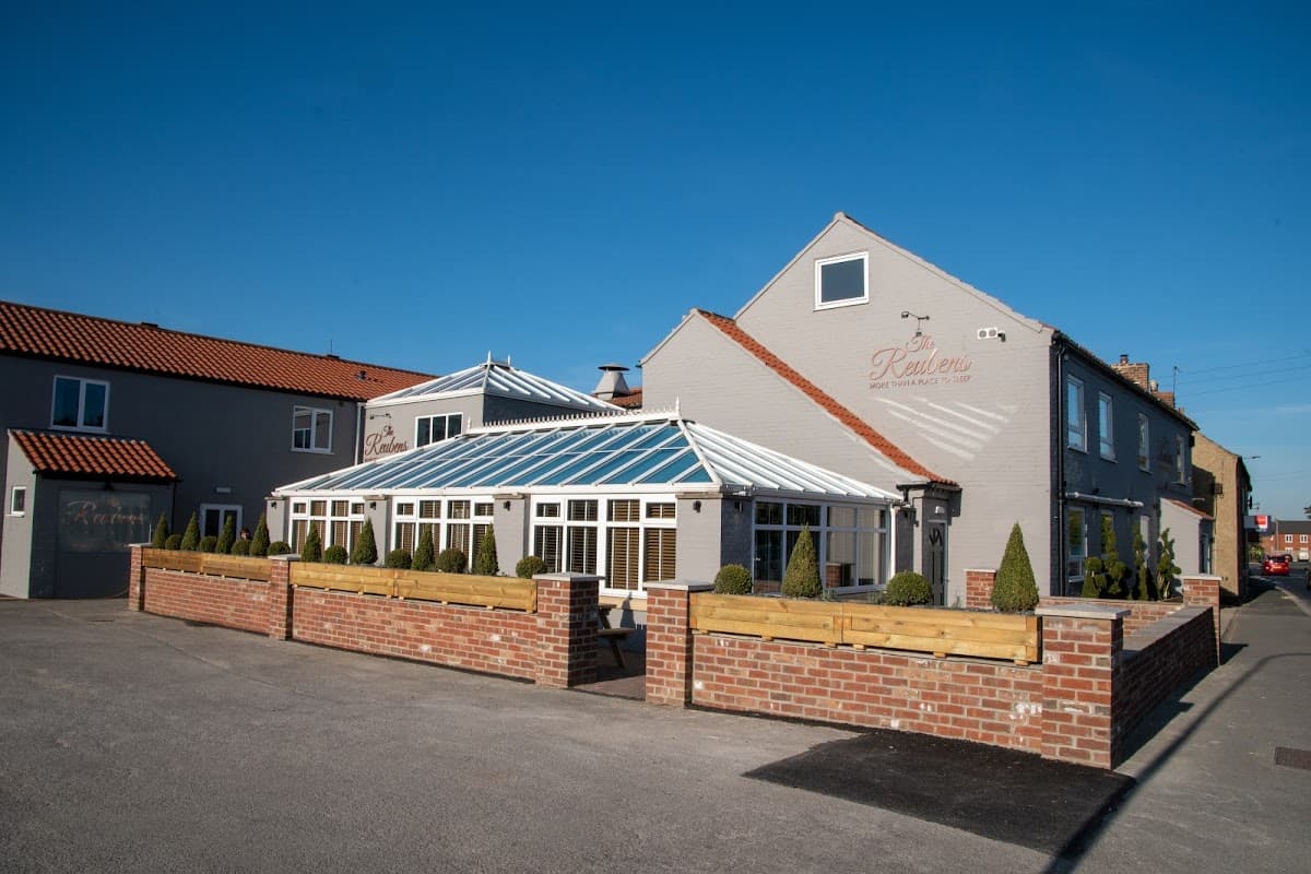 Quaint restaurant with a glass conservatory, surrounded by neatly trimmed hedges and a clear blue sky.