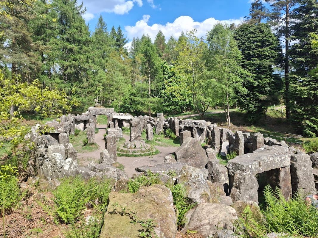 Ancient stone structure surrounded by lush greenery and trees under a blue sky with scattered clouds.