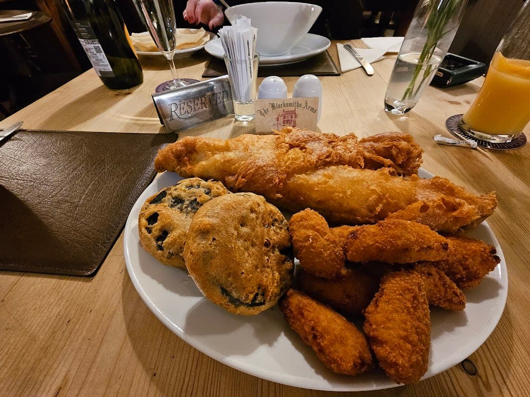 Plate of fish and chips with crispy batter, alongside two cookies and chicken nuggets on a wooden table.