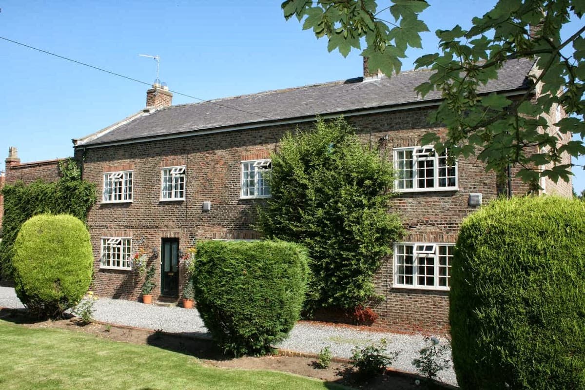 Charming brick manor house surrounded by neatly trimmed hedges and a gravel pathway under a clear blue sky.