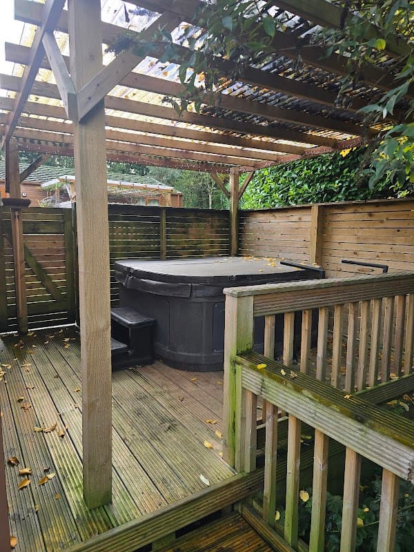 Hot tub under a wooden pergola, surrounded by wooden fencing and greenery at Croft Park Holiday Lodges.