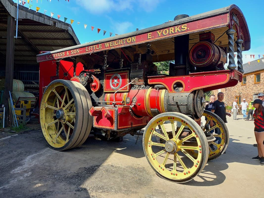 Vintage steam engine with bright red and yellow detailing, set against a backdrop of bunting and onlookers at a rally.