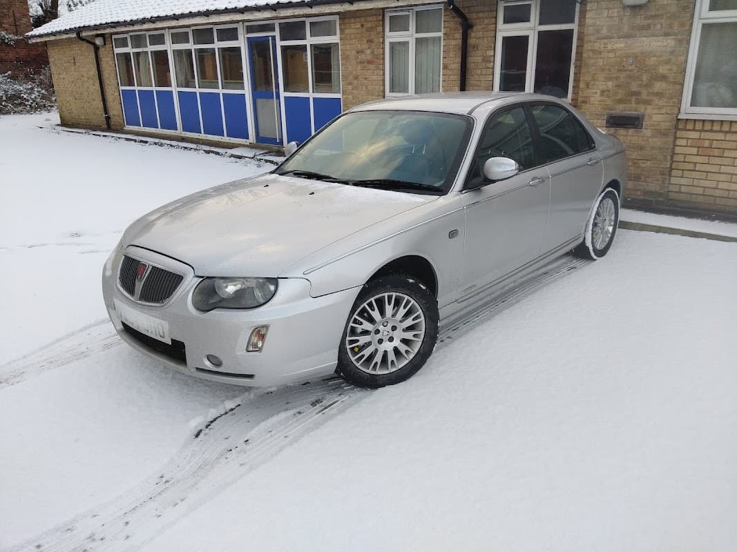 Silver car parked on snowy ground outside a brick building with windows in Little Weighton, Yorkshire.