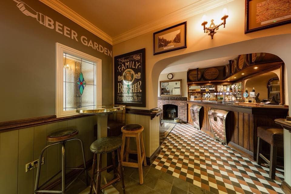 Cozy bar interior with wooden accents, checkered floor, and a stained glass window, featuring a welcoming atmosphere.