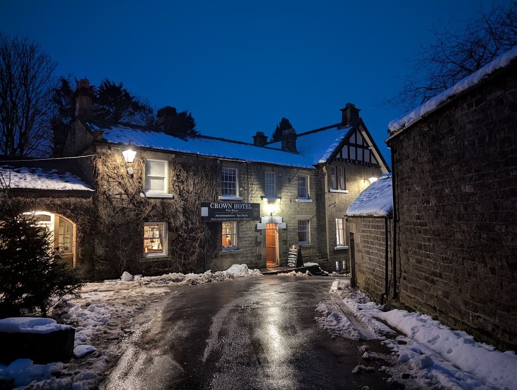 Crown Hotel in Lofthouse, North Yorkshire, with snow-covered ground and warm lights illuminating the entrance at dusk.