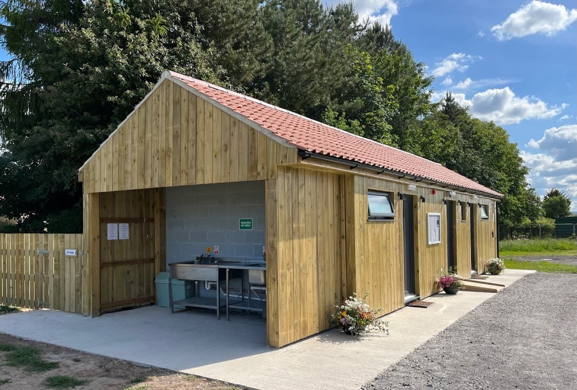 Wooden building with a red-tiled roof, surrounded by greenery, serving as facilities for Pheasant Hill Caravan Park.
