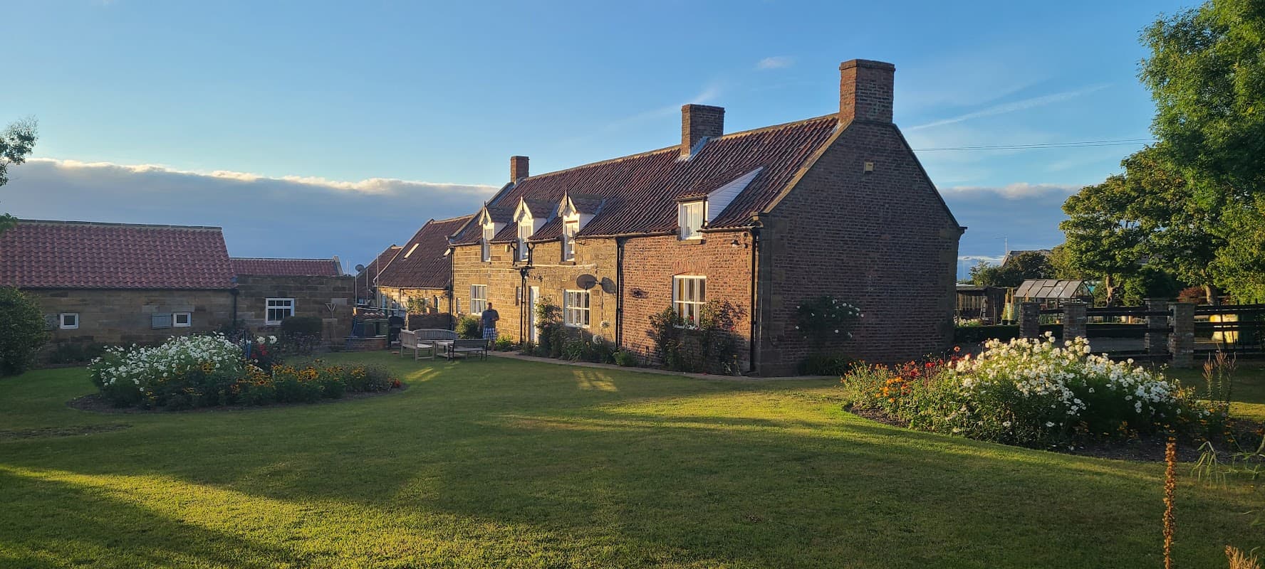 Quaint brick hotel surrounded by lush gardens and flower beds under a clear blue sky in Low Hawsker, Yorkshire.
