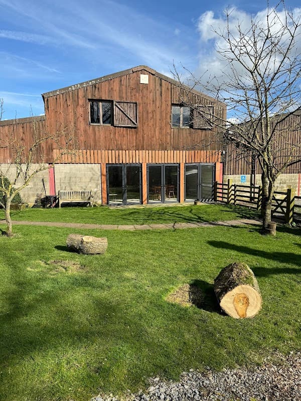 Rustic hotel building with wooden exterior, large windows, and grassy area featuring logs and trees in Low Row, Yorkshire.