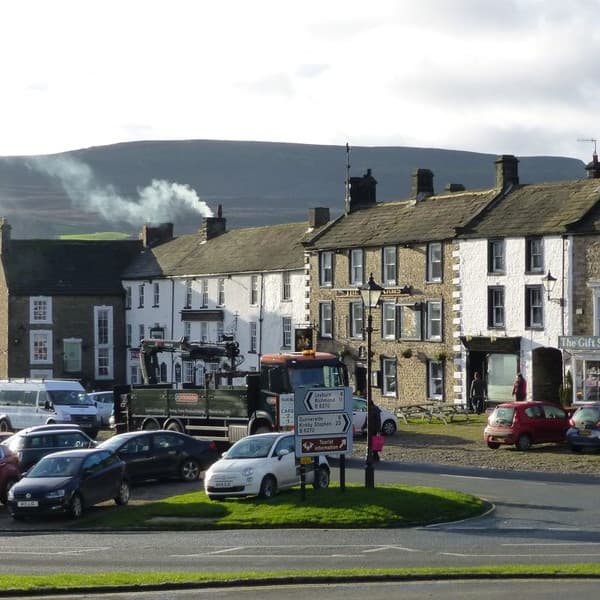 Historic stone buildings of Low Row Bunk Barns, surrounded by parked cars and rolling hills in the background.