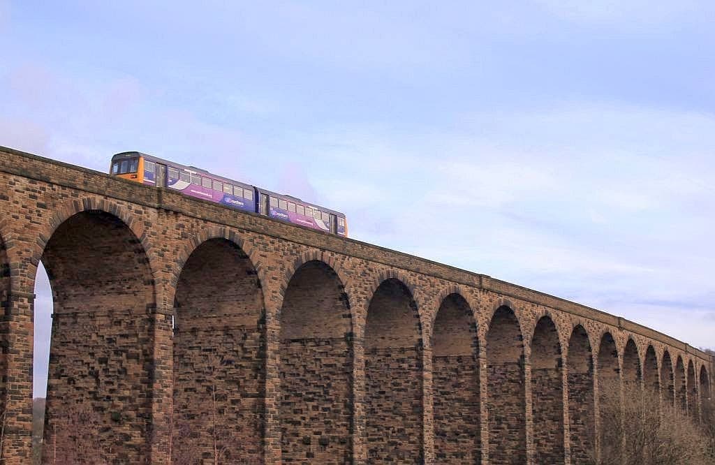 Historic stone viaduct with arches, featuring a train passing overhead against a blue sky.
