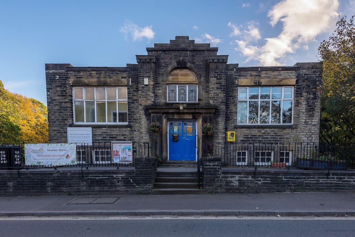 Luddenden Foot Community Centre features a stone facade, large windows, and a blue door, surrounded by trees.