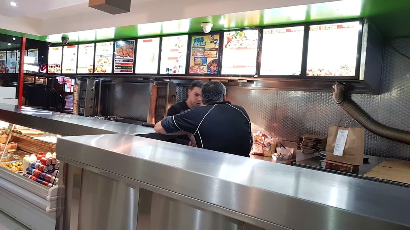 Takeaway counter at Maltby Charcoal Grill, featuring menu boards, food displays, and a customer interacting with staff.