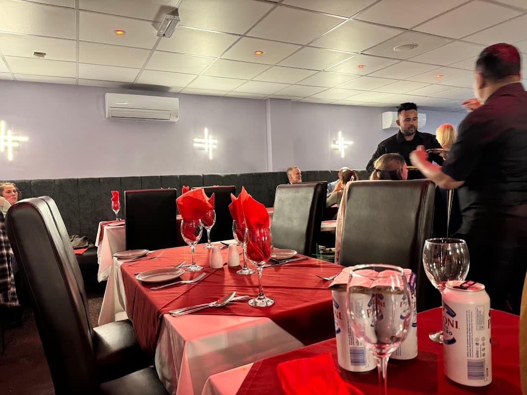 Tables with red and white tablecloths set for dining, featuring wine glasses and red napkins, in a lively restaurant setting.