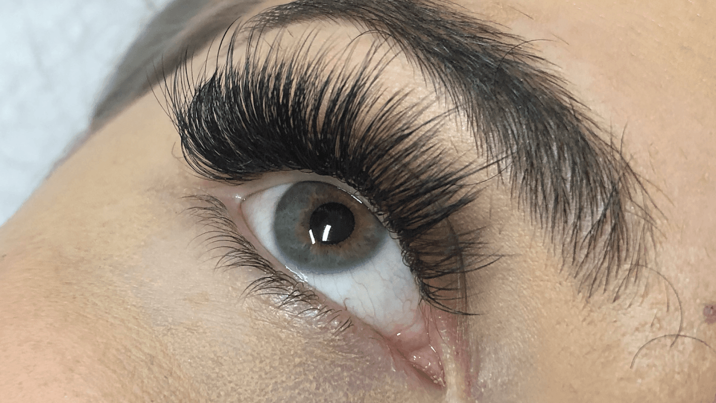Close-up of an eye with long, dramatic eyelashes and a green iris, showcasing detailed makeup artistry.