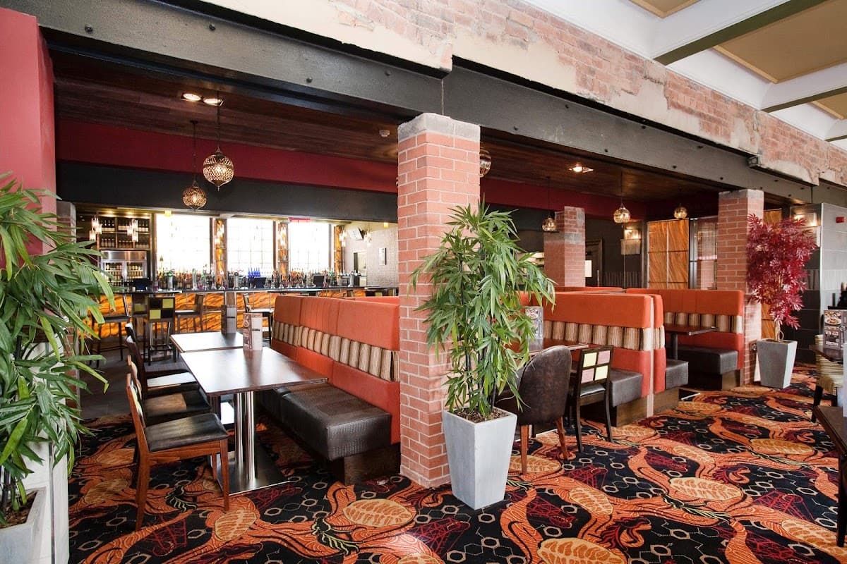 Interior of The Queens Hotel with vibrant carpet, cozy booths, and a bar in the background. Green plants add decor.