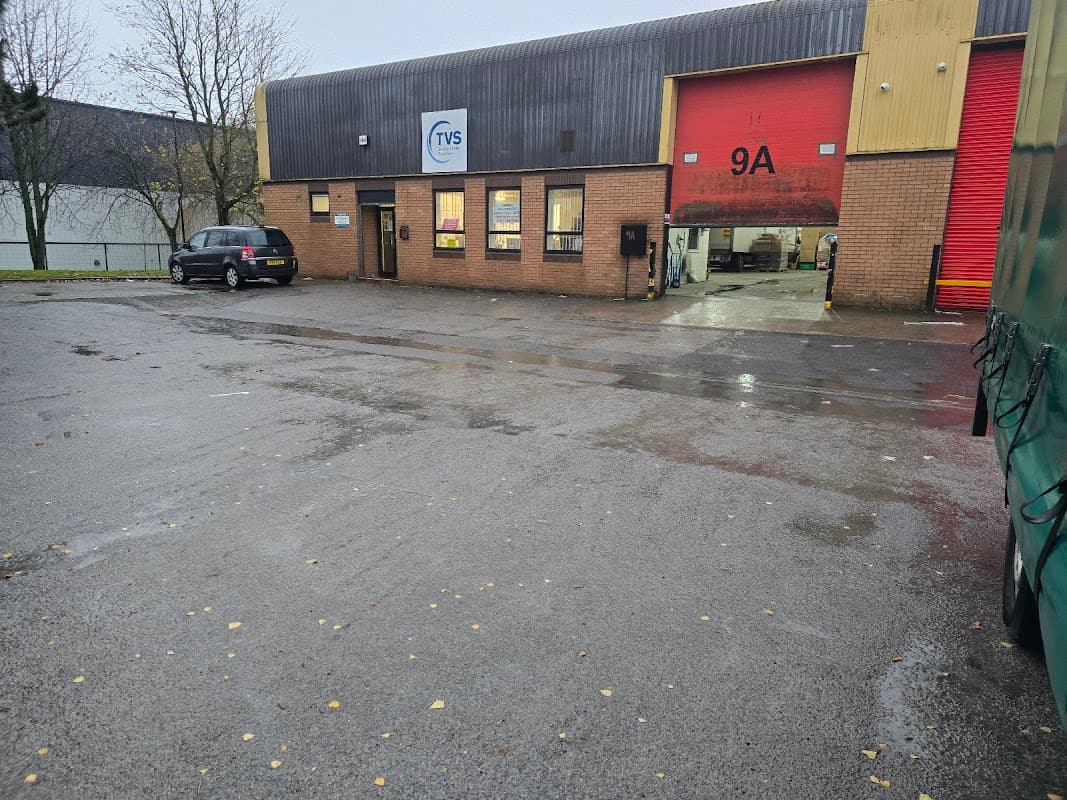 TVS SCS Courier Services building with red garage door, parked car, and wet ground in Maltby, Yorkshire.