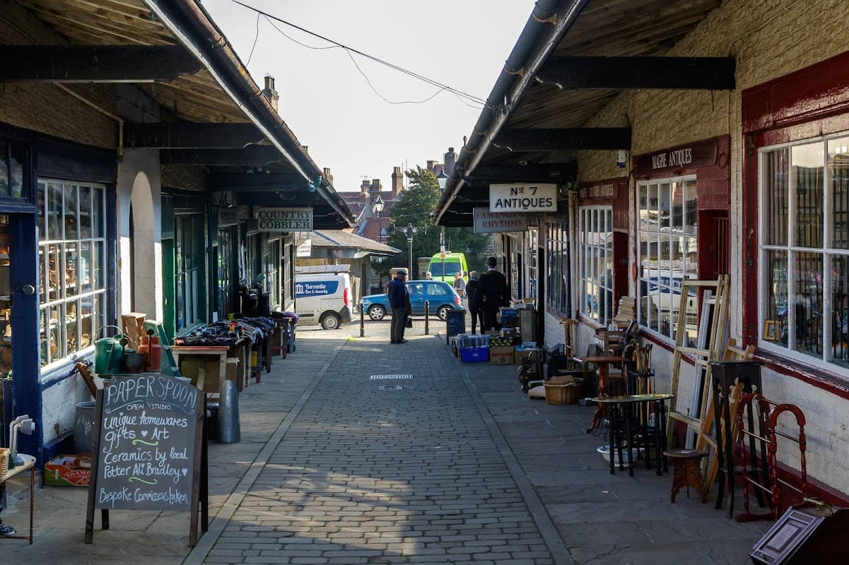 Shambles Car Park in Malton, Yorkshire, featuring shops, antiques, and a cobbled walkway under a covered arcade.