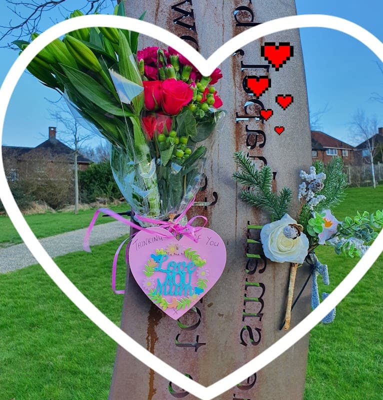 A heart-shaped frame surrounds a bouquet and a decorative heart tag at Castle View Park, with greenery and blue sky in the background.